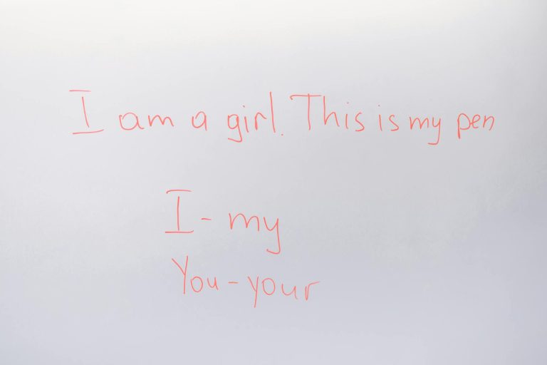 Handwritten English lesson on whiteboard with sentences and pronouns.